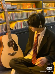 a man sitting in front of a guitar with headphones on his ears and wearing a suit