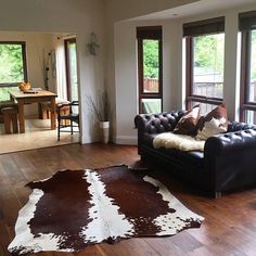 a living room filled with lots of furniture next to two large windows and a cowhide rug on the floor