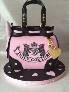 a pink and black purse cake with a gold heart on the front, sitting on top of a white table