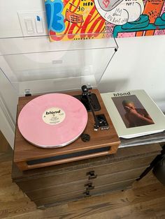 a record player sitting on top of a wooden table next to a wall with a painting behind it