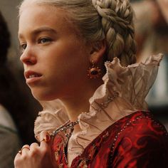 a woman with blonde hair wearing a red dress and gold earrings, looking off to the side