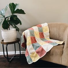 a couch with a crocheted blanket on it next to a potted plant