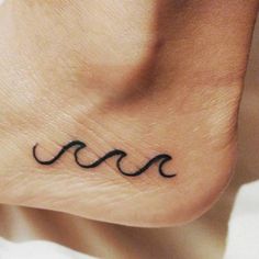 a small black wave tattoo on the side of a person's foot and it is written in cursive writing