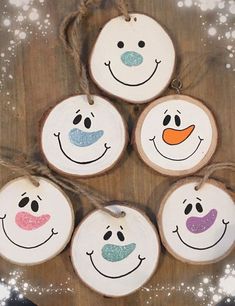 four wood slices with painted faces hanging from strings on a wooden board covered in snow