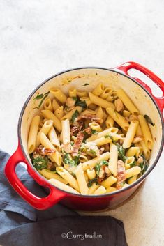 a red pot filled with pasta and meat on top of a white counter next to a blue towel