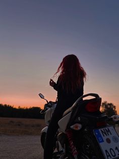 a woman with red hair is sitting on a motorcycle at sunset, looking off into the distance