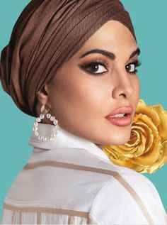 a woman wearing a brown turban and gold earrings with a rose in her hair