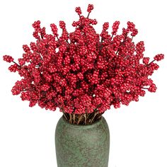 a green vase filled with red berries on top of a table