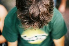 the back of a man's head wearing a green shirt and holding a cell phone