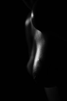 a black and white photo of a woman's breast in the dark, with light coming from behind her