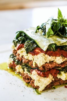 a stack of food sitting on top of a white plate covered in sauce and greens