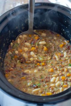 a pot filled with beans and vegetables on top of a table next to a spoon