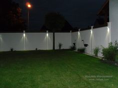 a fenced in yard with lights on the top of it and grass around it