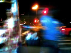 blurry photograph of people walking across the street at night with traffic lights in the background