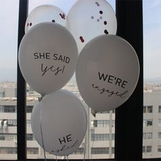 white balloons with words written on them are in front of a window that reads she said yes, we're engaged