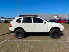 a white suv parked in a parking lot with other cars behind it and an empty bleachers