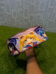 a person's hand holding up a wristband with anime characters on it in front of a wall