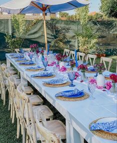 an outdoor table set with blue and white plates, place settings and flowers on it