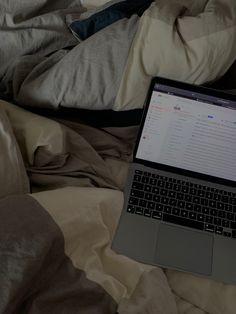 an open laptop computer sitting on top of a bed covered in sheets and blankets,