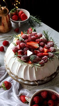 a cake covered in frosting and strawberries next to bowls of berries on a table