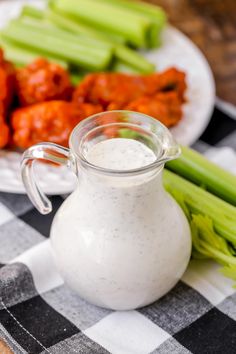 a plate with celery sticks next to a small glass pitcher filled with ranch dressing