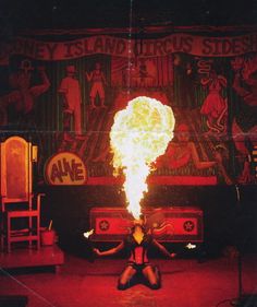 a woman sitting on the ground with fire in her hand and an advertisement behind her