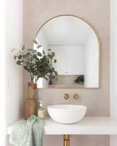 a white sink sitting under a mirror next to a vase with a plant in it