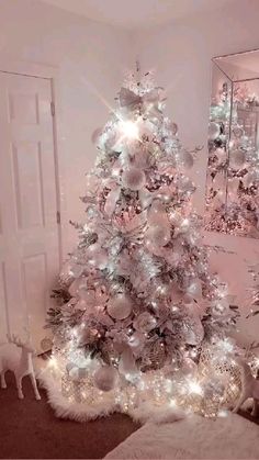 a white christmas tree with silver ornaments and lights in a living room next to a mirror