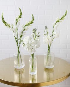 three clear vases with white flowers on a gold table