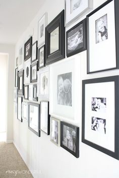 a wall full of black and white pictures with frames on the wall next to it