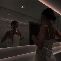 a woman standing in front of a bathroom mirror looking at herself in the mirror,