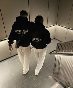 two people wearing black sweatshirts walking down an escalator in a public building