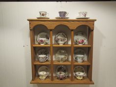 a wooden shelf filled with plates and cups on top of it's sides in front of a white wall