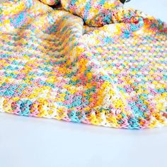 a colorful crocheted blanket laying on top of a white table next to a pair of scissors