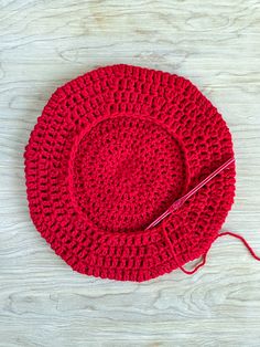 a red crocheted hat sitting on top of a wooden table next to a pair of scissors