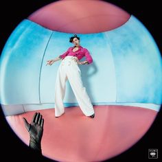 a woman in white pants and pink shirt standing next to a giant blue ball with her hands on the ground