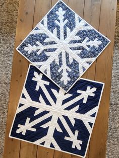 two quilted snowflakes sitting on top of a wooden floor