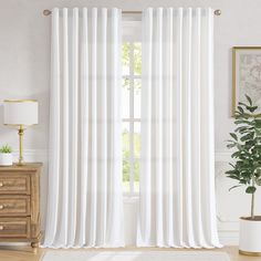 a white curtain hanging in front of a window with a potted plant next to it