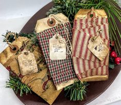 three christmas gift bags with tags on them sitting on a wooden platter surrounded by greenery