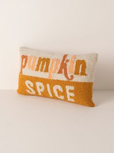 an orange and white pillow with the words pumpkin spice on it, sitting on a table