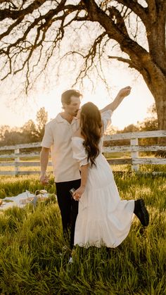 a man and woman standing in the grass with their arms around each other as they hold hands