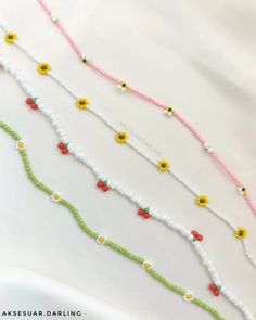 three strands of beaded necklaces with yellow and red flowers on white fabric background