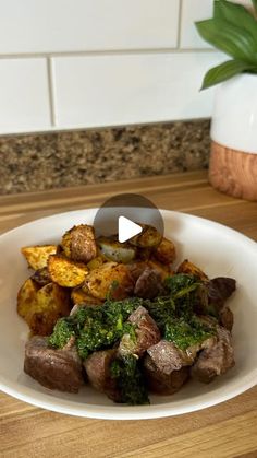 a white plate topped with potatoes and broccoli next to a potted plant