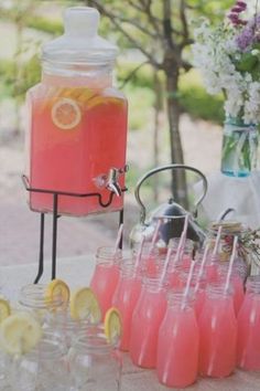 a table topped with lots of glasses filled with pink liquid and lemons next to a beverage dispenser