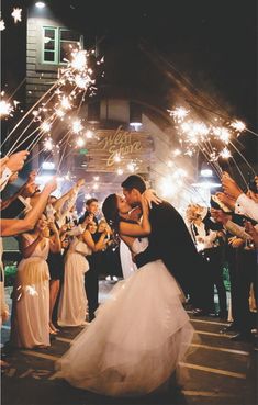 a bride and groom kissing in front of their guests with sparklers at night time