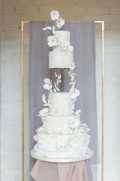 a wedding cake with white flowers on top is displayed in front of a purple backdrop