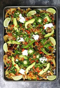 a tray filled with nachos topped with sour cream and avocado wedges