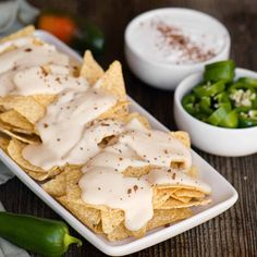 nachos with white sauce and green peppers on a plate next to small bowls