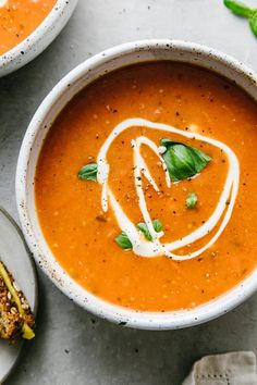 two bowls of tomato soup on a table with bread and basil garnishes