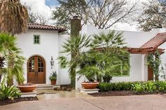 a white house with palm trees and potted plants in front of the entrance to it